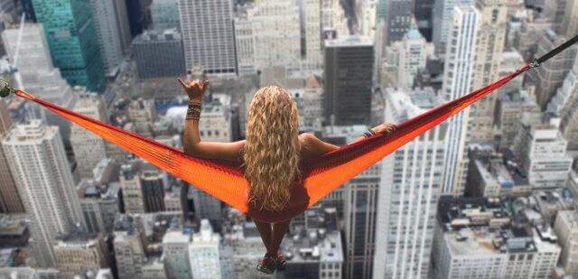 Woman relaxing in an orange hammock suspended high above a city skyline