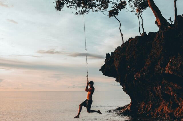 Man hanging from rope over water