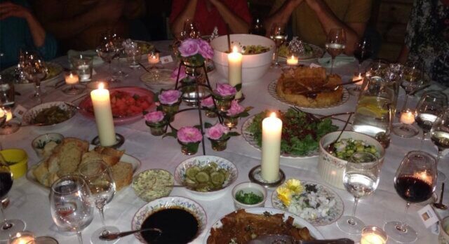 The candlelit table at my Gratitude Dinner, set with pink roses, shared dishes and wine glasses, with guests gathered around.