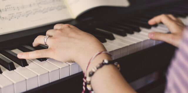 Hands playing a piano with sheet music open above the keys — feeling what the music does to your energy