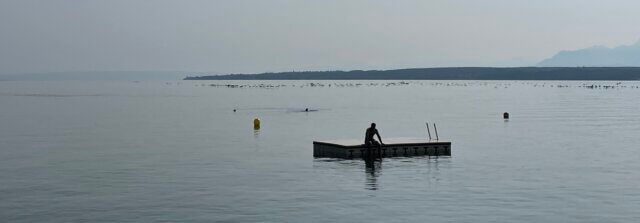 A person sits alone on a floating platform on a calm, misty lake, pausing in stillness.