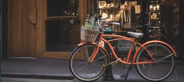 Orange bicycle with a wicker basket of plants parked outside a shop window — an ordinary errand that carried a lesson